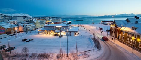 A snow-covered town with buildings, a road, and a body of water in the background.