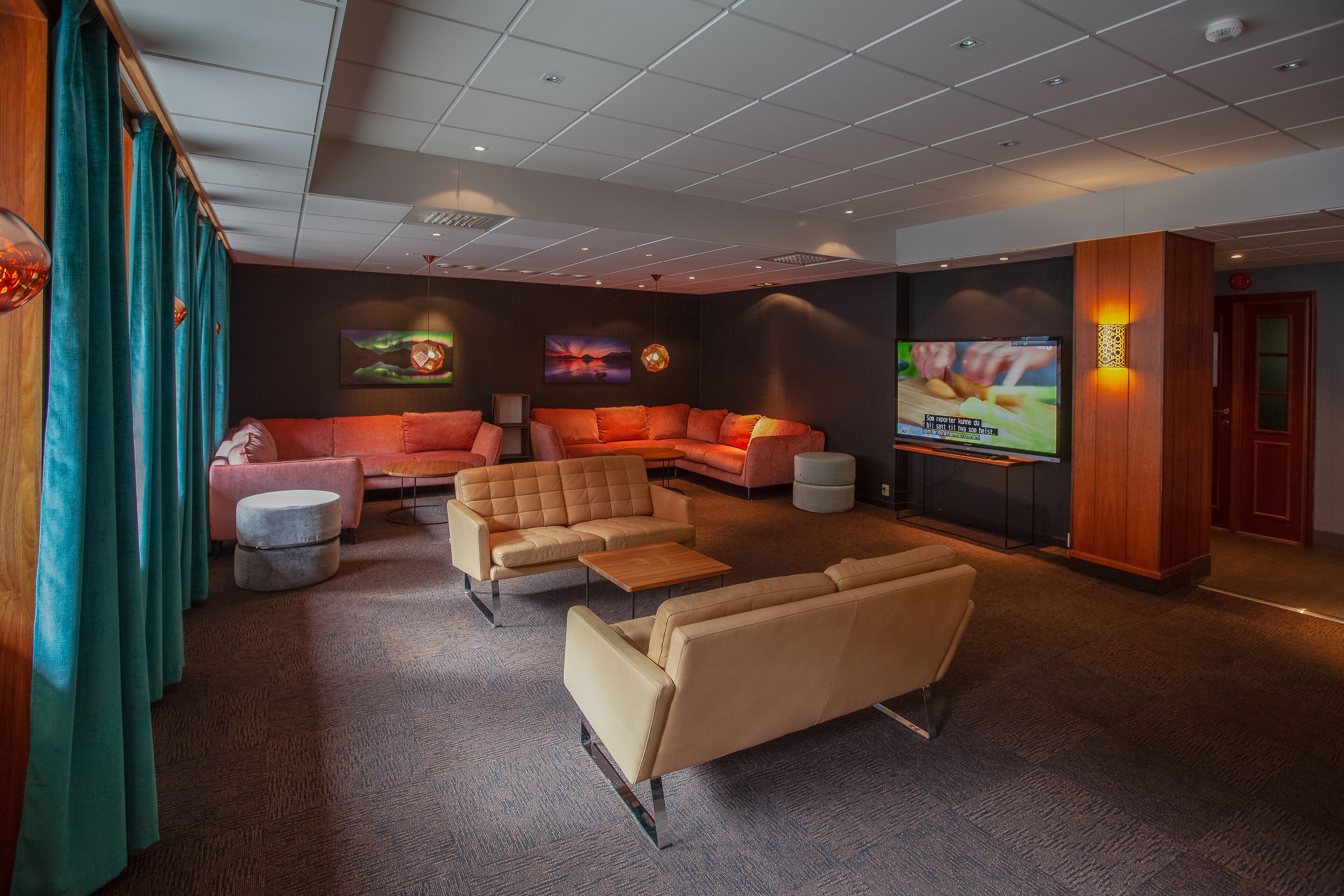 A modern lounge area with sofas, ottomans, and a flat-screen TV.