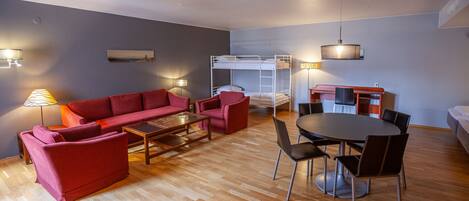 A compact living space with a sofa, armchairs, a coffee table, a dining table with chairs, a bunk bed, and a lamp.