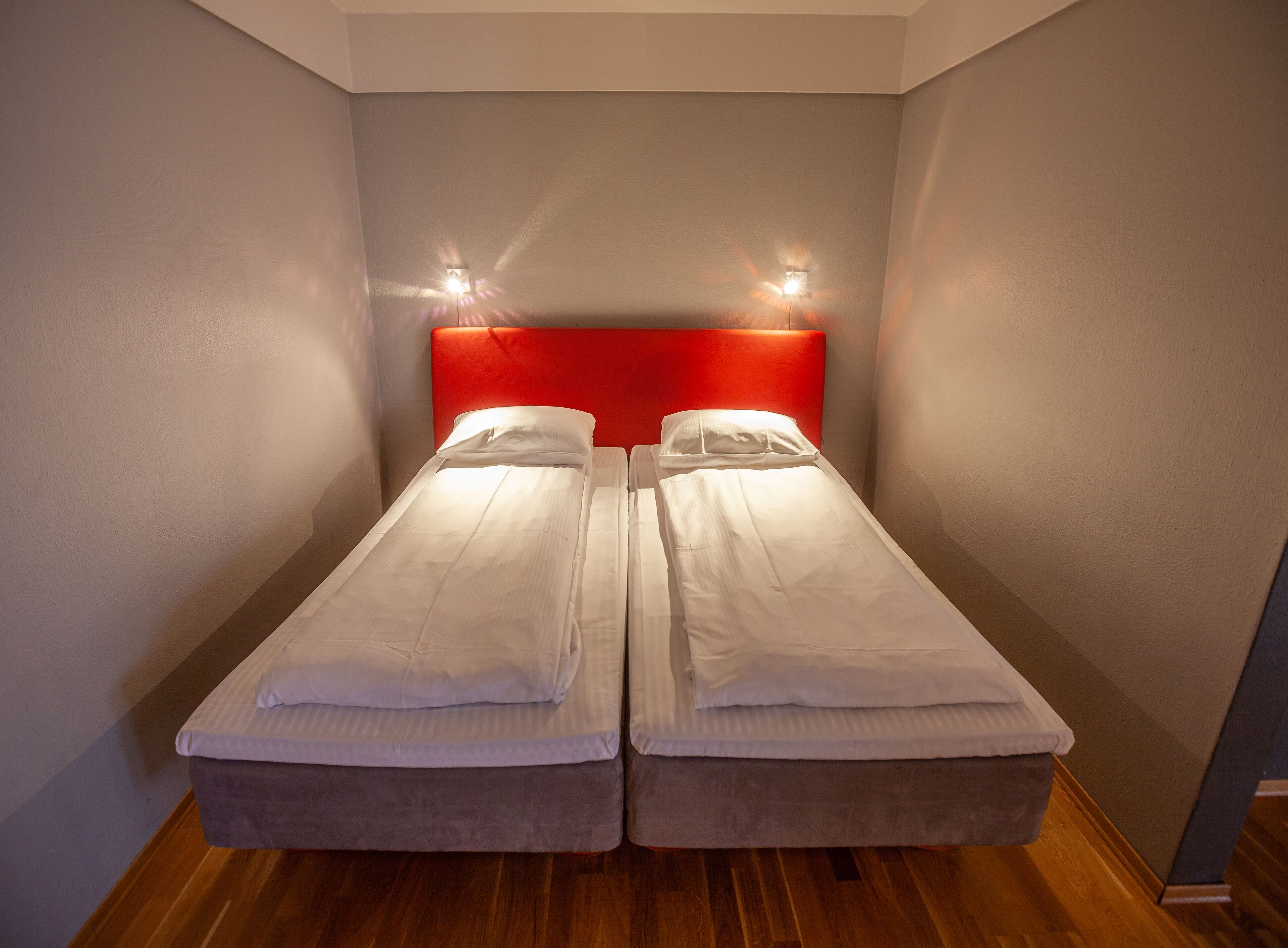 A twin room with two single beds, a red headboard, and a wooden floor.