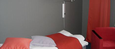 Habitación de hotel con una cama, una silla roja, una lámpara y un cuadro en la pared.