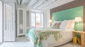 A bedroom with a bed, two bedside lamps, a wooden nightstand, a green headboard, and a sliding glass door leading to a balcony.