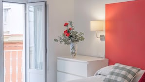 A bedroom with a bed, a nightstand, a vase with flowers, a lamp, and a view through a door.