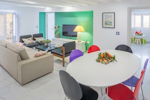 A modern living room with a sofa, chairs, a TV, a table with a plant, and a green accent wall.
