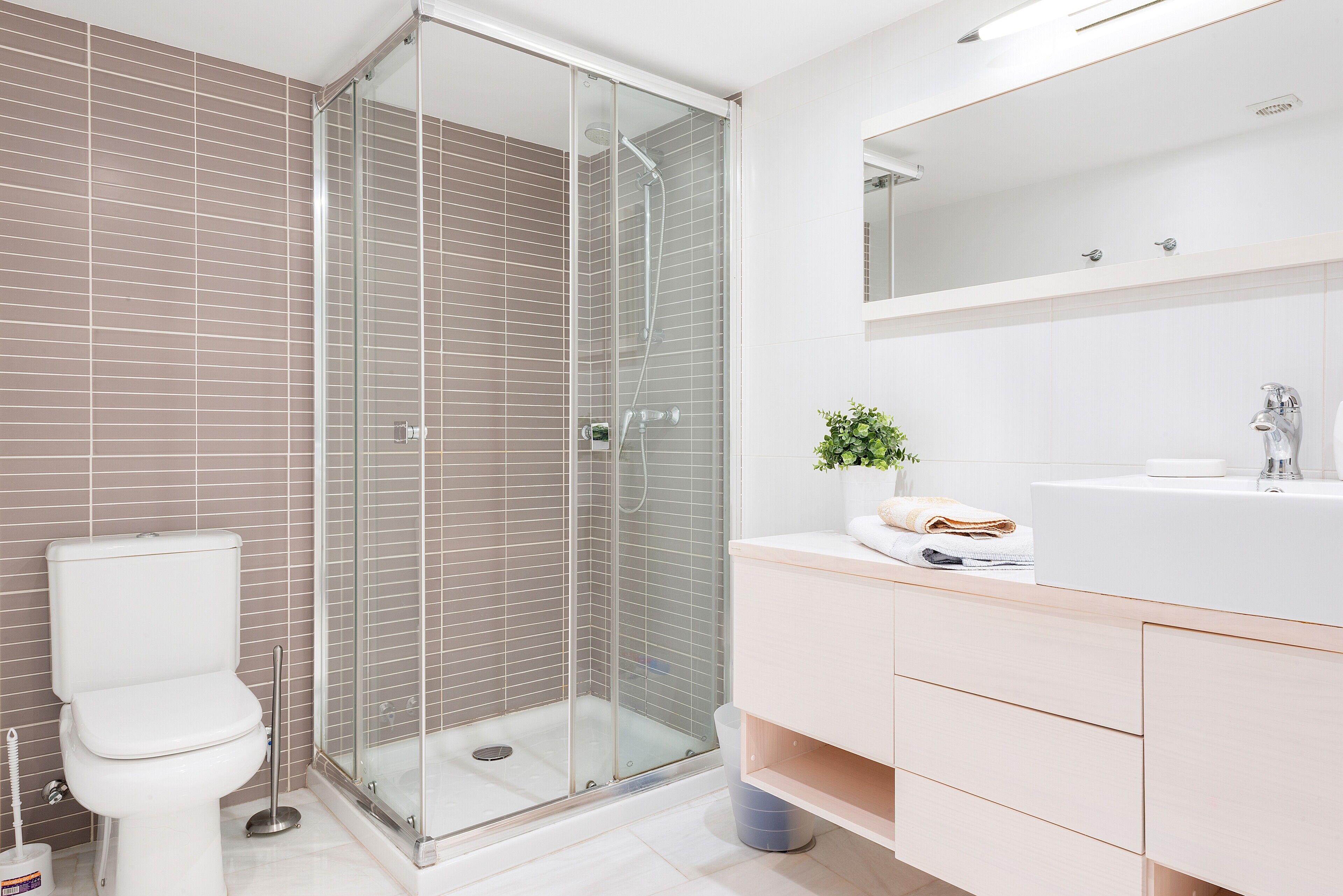 A bathroom with a glass-enclosed shower, a white toilet, and a sink with a mirror above it.