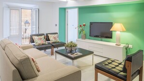A living room with a sofa, two armchairs, a coffee table, a TV, and a lamp.