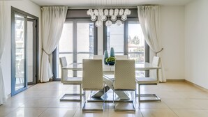 A modern dining area with a glass table, four chairs, and a hanging light fixture. - Kook 7 Apartment - Isrentals (Jerusalem)