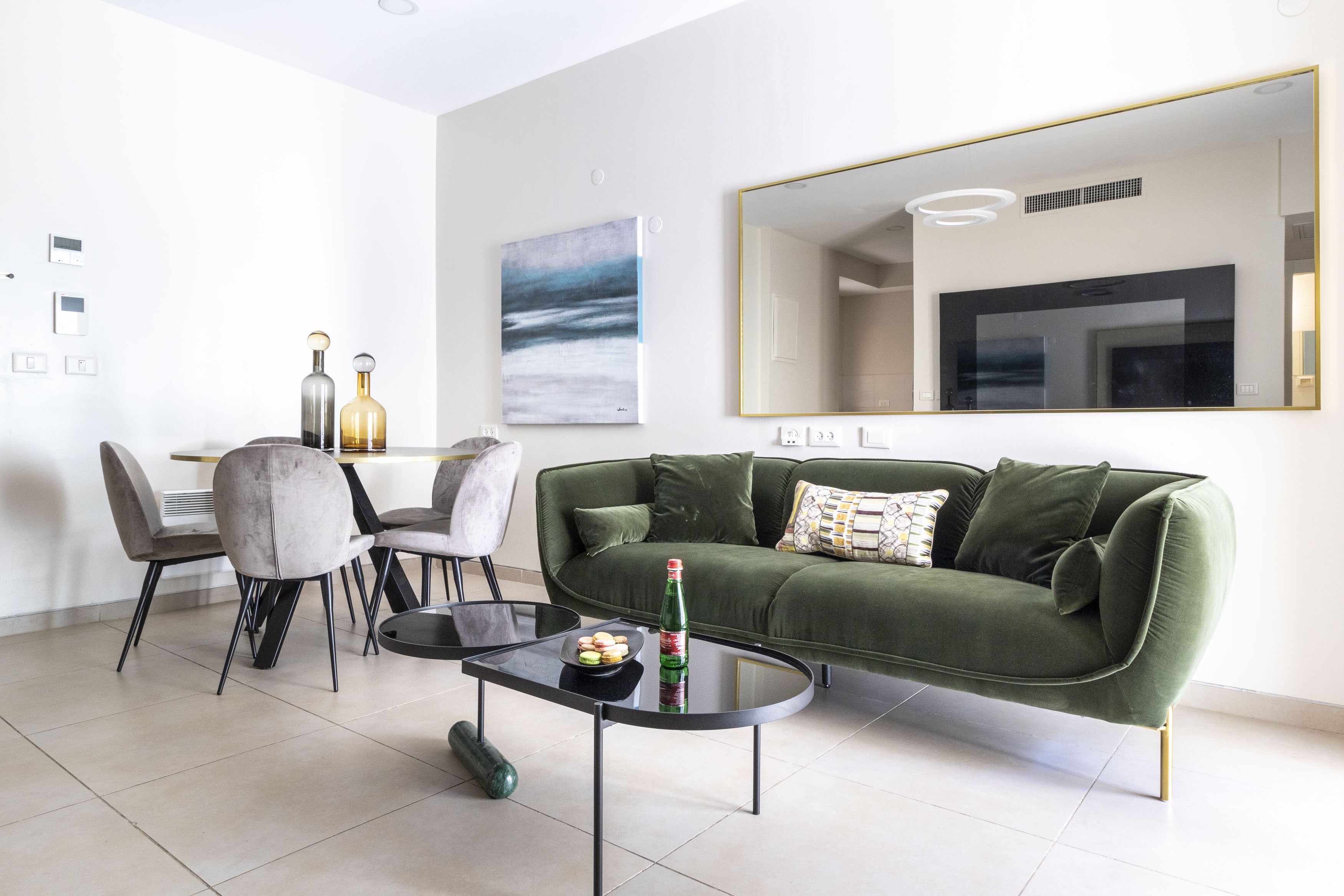 Una sala de estar moderna con un sofá verde, una mesa de comedor con sillas y un espejo grande en la pared.