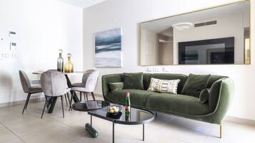 Una sala de estar moderna con un sofá verde, una mesa de comedor con sillas y un espejo grande en la pared.