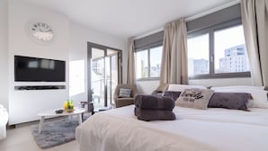 A modern hotel room with a large bed, a flat-screen TV, a small table with a bowl and bottles, and a view of the city through the window. - Kook 7 Apartment - Isrentals (Jerusalem)