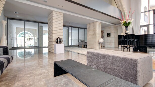 A modern lobby with a marble floor, a reception desk, and a seating area with a bench and chairs. - Kook 7 Apartment - Isrentals (Jerusalem)