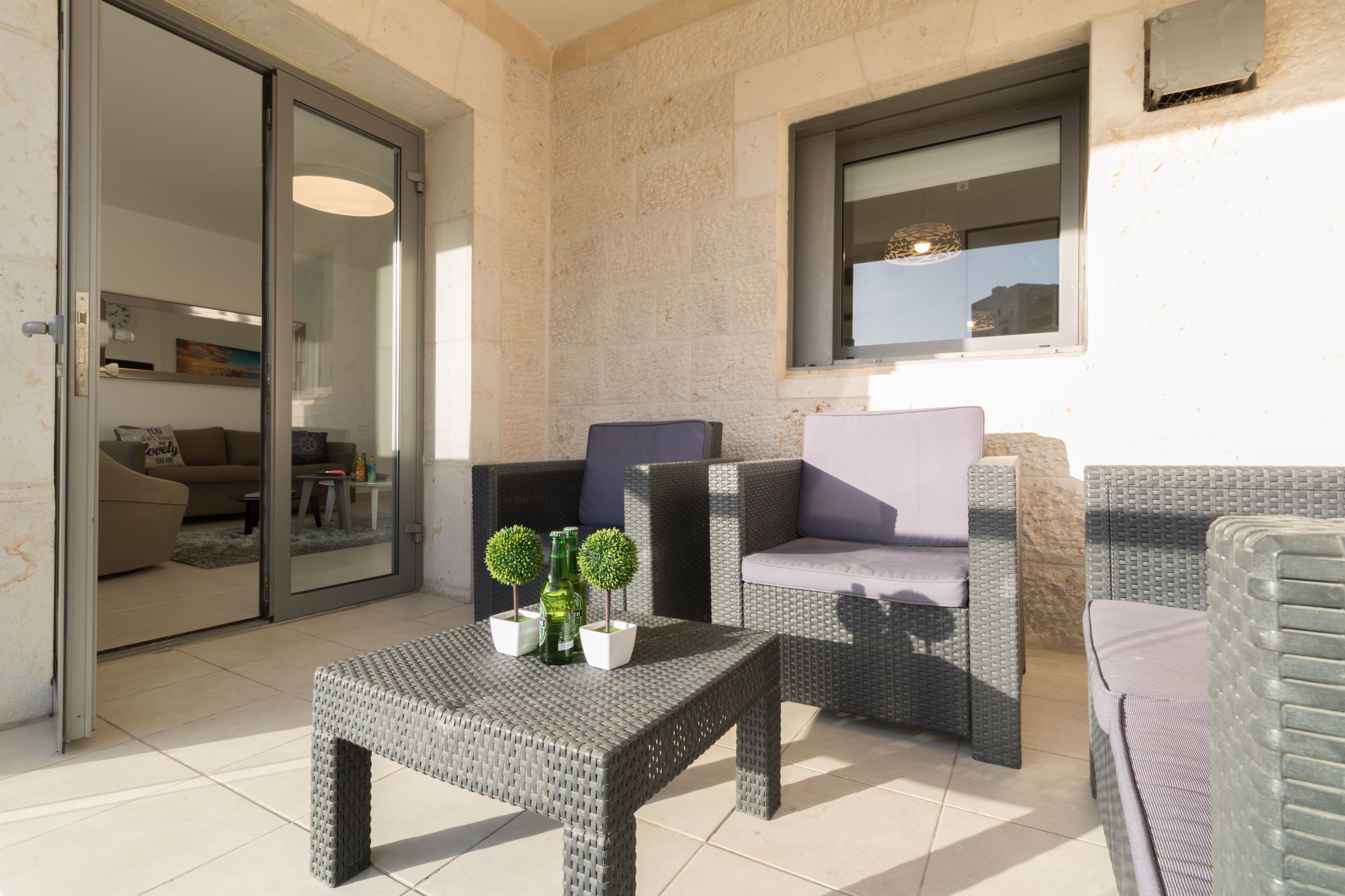 Un balcón con mobiliario de mimbre, una puerta de vidrio que da a un espacio interior y una ventana con vistas.