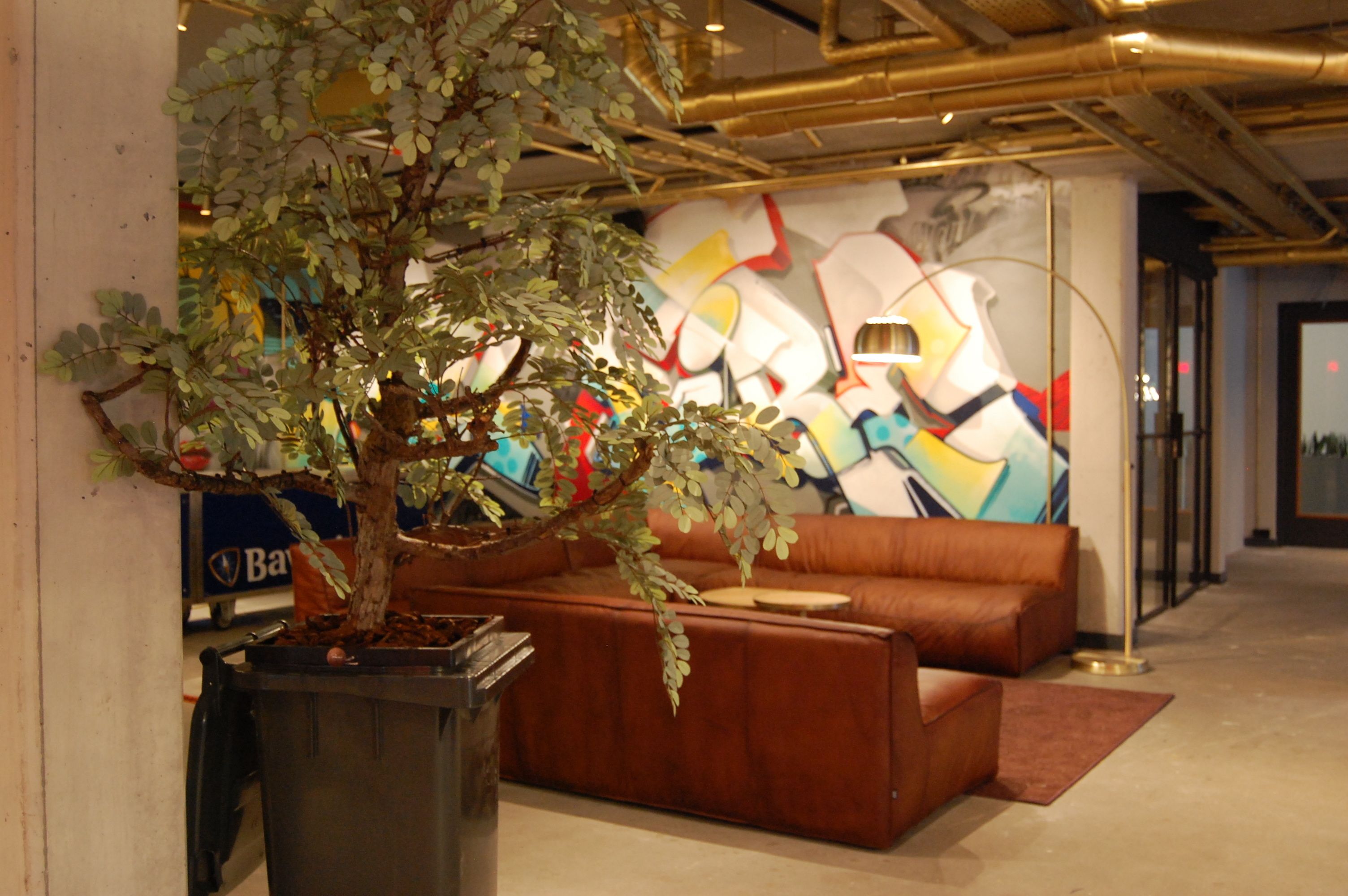 Um hall moderno com uma grande árvore artificial, um sofá de couro marrom e um mural abstrato colorido na parede.
