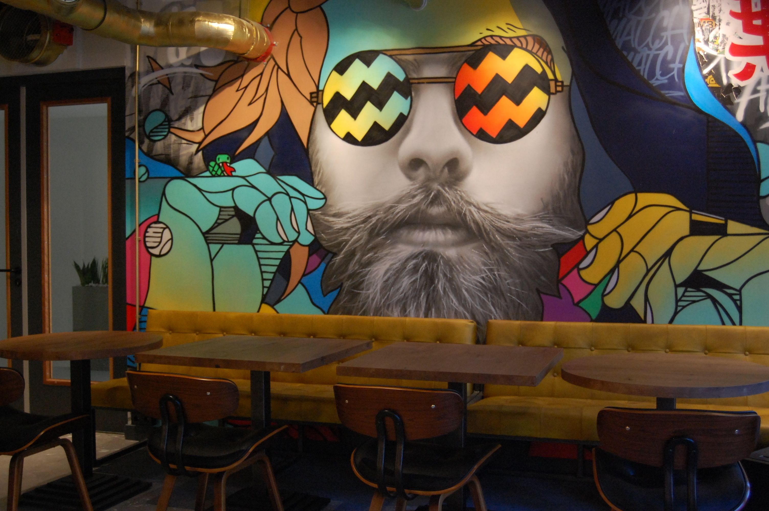 Interior de restaurante con un mural de un personaje de caricatura, mesas y sillas de madera.