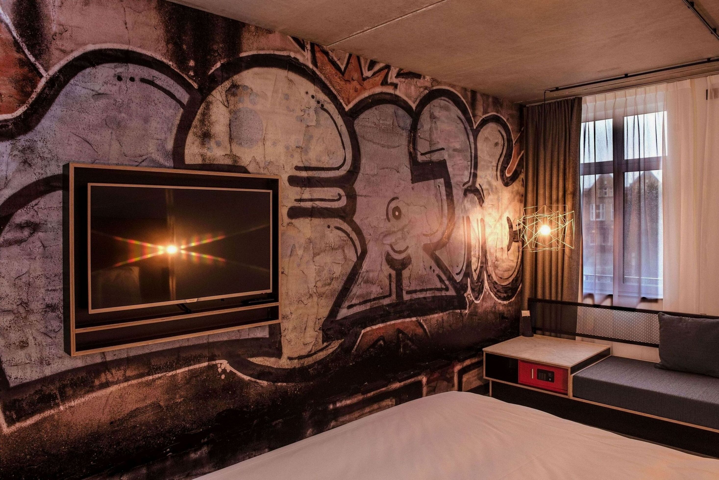 A modern bedroom with graffiti art on the wall, a TV, and a window with curtains.