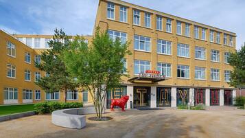 A hotel with a yellow facade, multiple windows, and a red lion statue in the entrance.