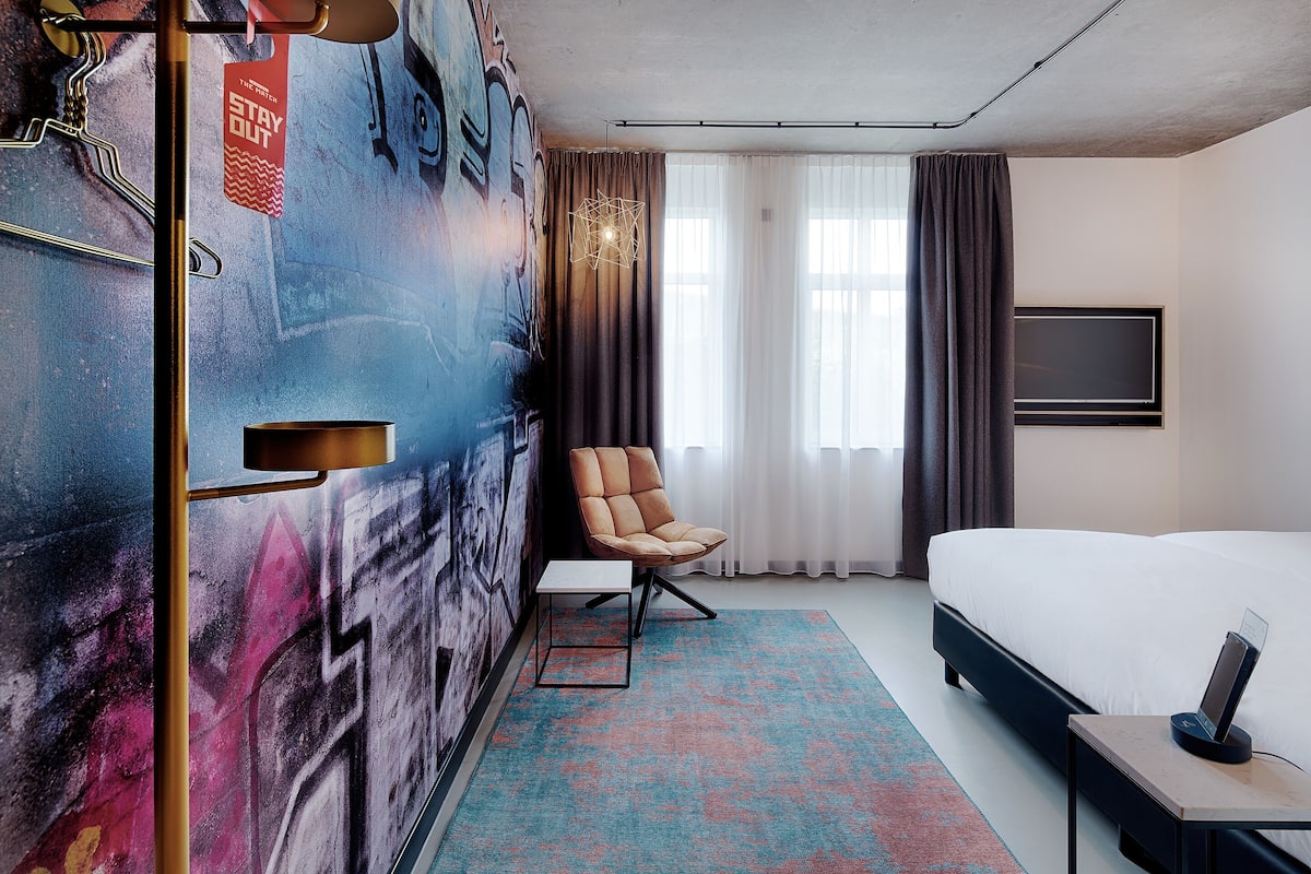 Una habitación de hotel con una cama, una silla, un escritorio, un televisor y una pared con grafitis.