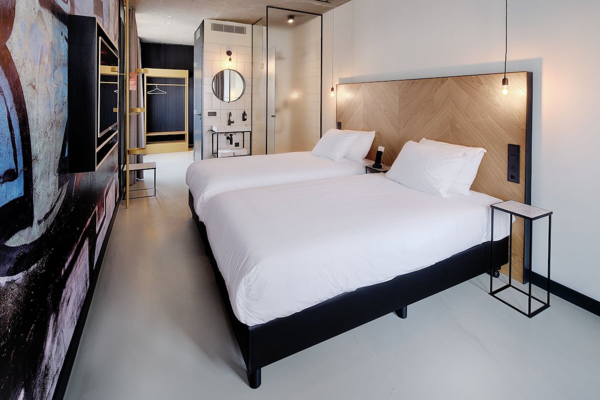 Una habitación de hotel moderna con una cama grande, una mesita de noche, un espejo y un armario.