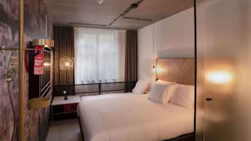 A modern hotel room with a large bed, a desk, and a window with curtains.