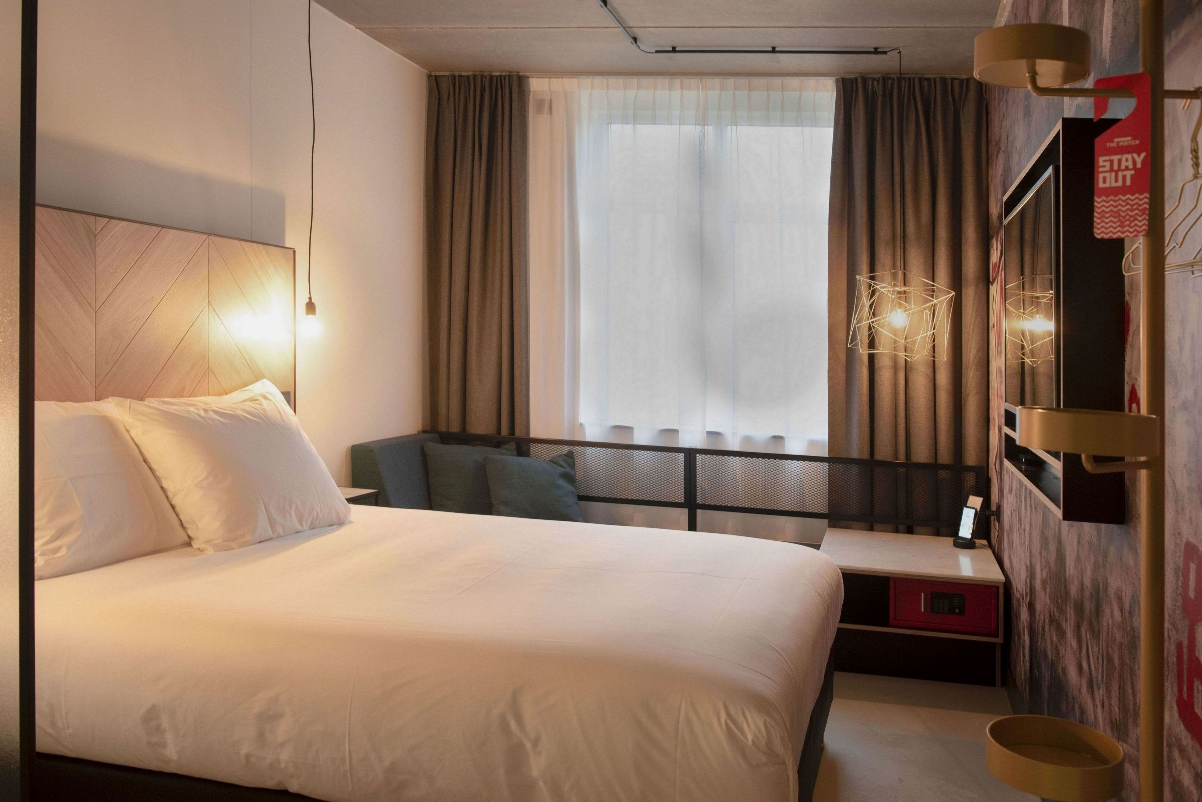 Una habitación de hotel con cama, escritorio, silla, ventana con cortinas y televisor montado en la pared.