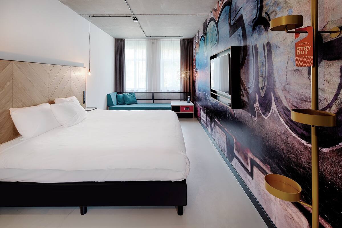 Una habitación de hotel moderna con una cama grande, un área de descanso, un televisor y un mural.