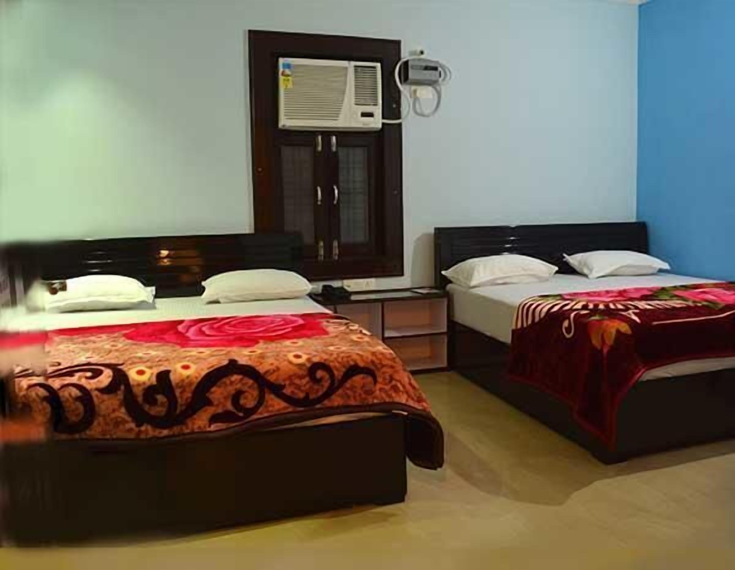 A hotel room with two beds, a nightstand, an air conditioning unit, and a wall-mounted lamp.