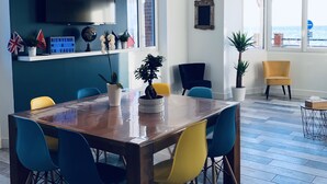 Un área de comedor moderna con una mesa de madera y sillas coloridas, un televisor sobre la mesa y plantas en macetas en el alféizar de la ventana.
