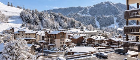 A snow-covered resort with multiple buildings, a parking area, and a mountainous backdrop.