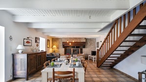 A spacious dining area with a high ceiling, stone fireplace, and a wooden staircase.