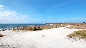 A sandy path leading to a beach with a wooden fence and a clear blue sky.