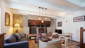 A cozy living room with a stone wall, a fireplace, wicker furniture, and a television.