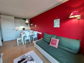 Ett kompakt bostadsutrymme med ett litet kök, en matplats och en soffa med mönstrade kuddar.