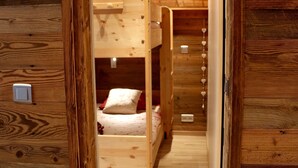 Una habitación de madera con literas, suelo de madera y una lámpara de techo blanca.