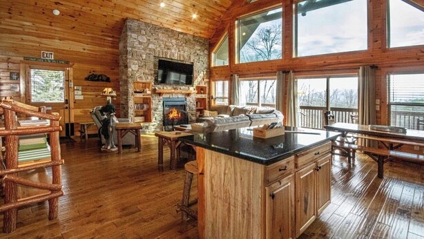 L’intérieur d’une cabane est agrémenté d’une cheminée en pierre, de meubles en bois et de grandes fenêtres.