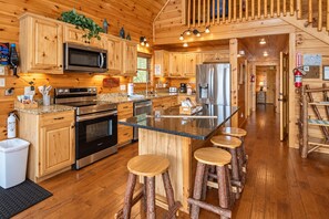 A modern kitchen with wooden cabinets, stainless steel appliances, a granite countertop, and a central island with stools. - Hot Tub, Fire Pit, Views, Wheelchair Accessible Retreat (Sevierville)