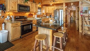 Une cuisine de style rustique, avec des éléments en bois, un îlot central, des tabourets de bar et un escalier menant à un niveau supérieur.