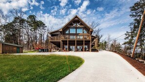 Une grande cabane en bois à deux étages, dotée d’une véranda qui fait le tour de la maison, entourée d’une pelouse bien entretenue et de grands arbres.