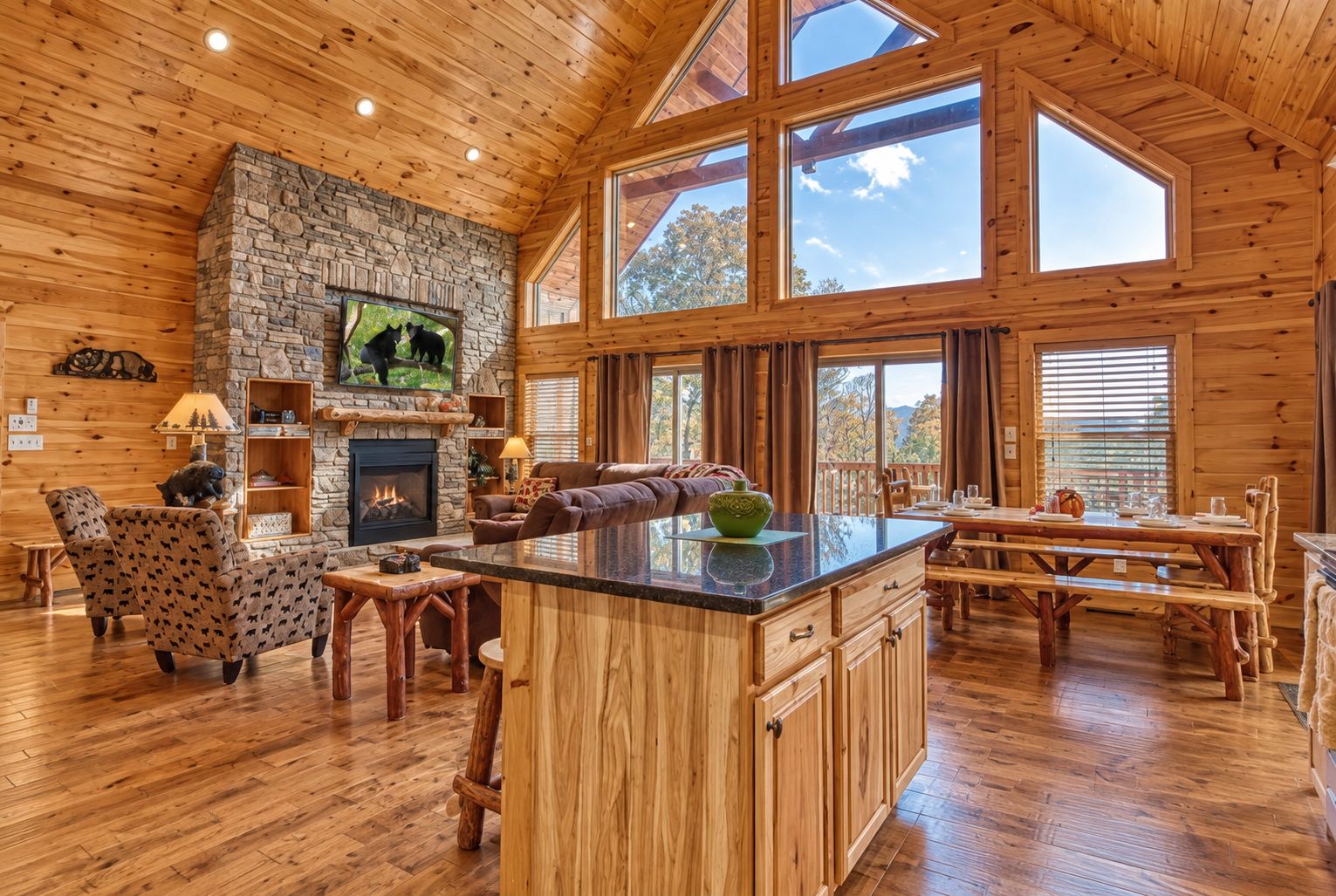A spacious cabin interior with a stone fireplace, wooden furniture, and large windows.
