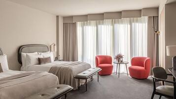 Habitación de hotel con dos camas, un banco, dos sillas rojas, una mesita y una lámpara.