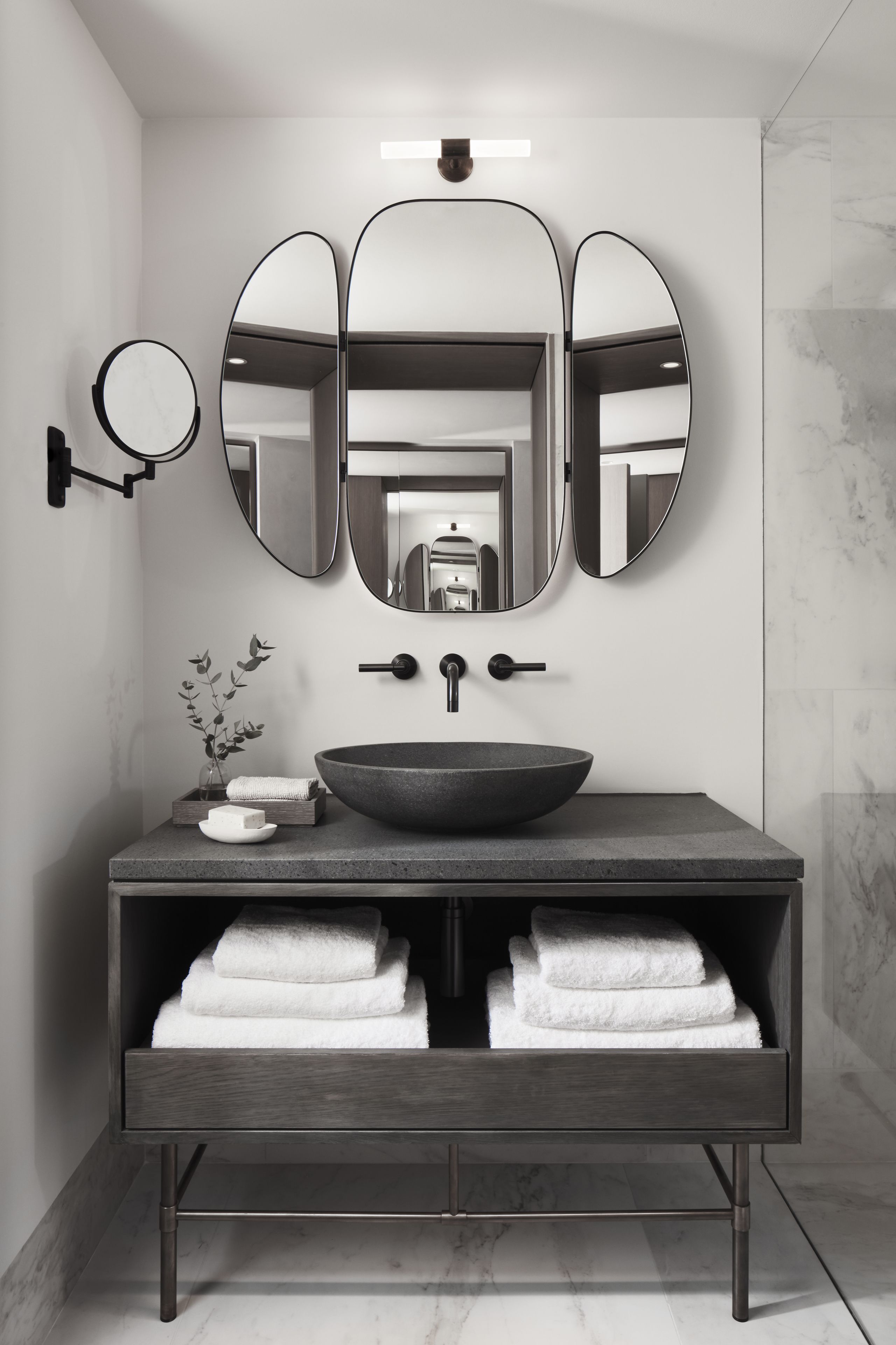 Un baño moderno con un espejo ovalado grande, un espejo redondo, un lavabo sobre encimera y un perchero con toallas dobladas.