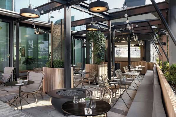 Un área de comedor al aire libre con mobiliario moderno, una chimenea y luces colgantes.