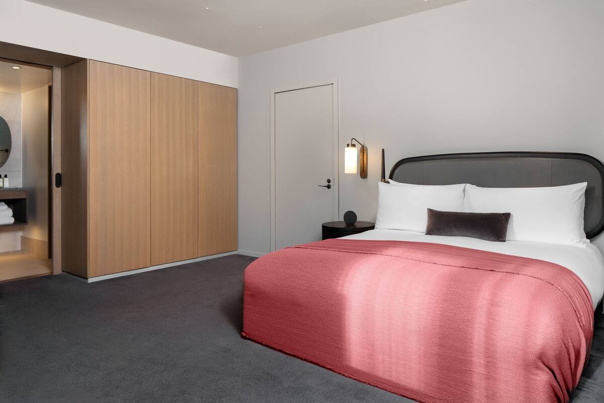 Moderni hotellihuone, jossa on suuri sänky, puinen vaatekaappi ja yöpöytä, jossa on lamppu.