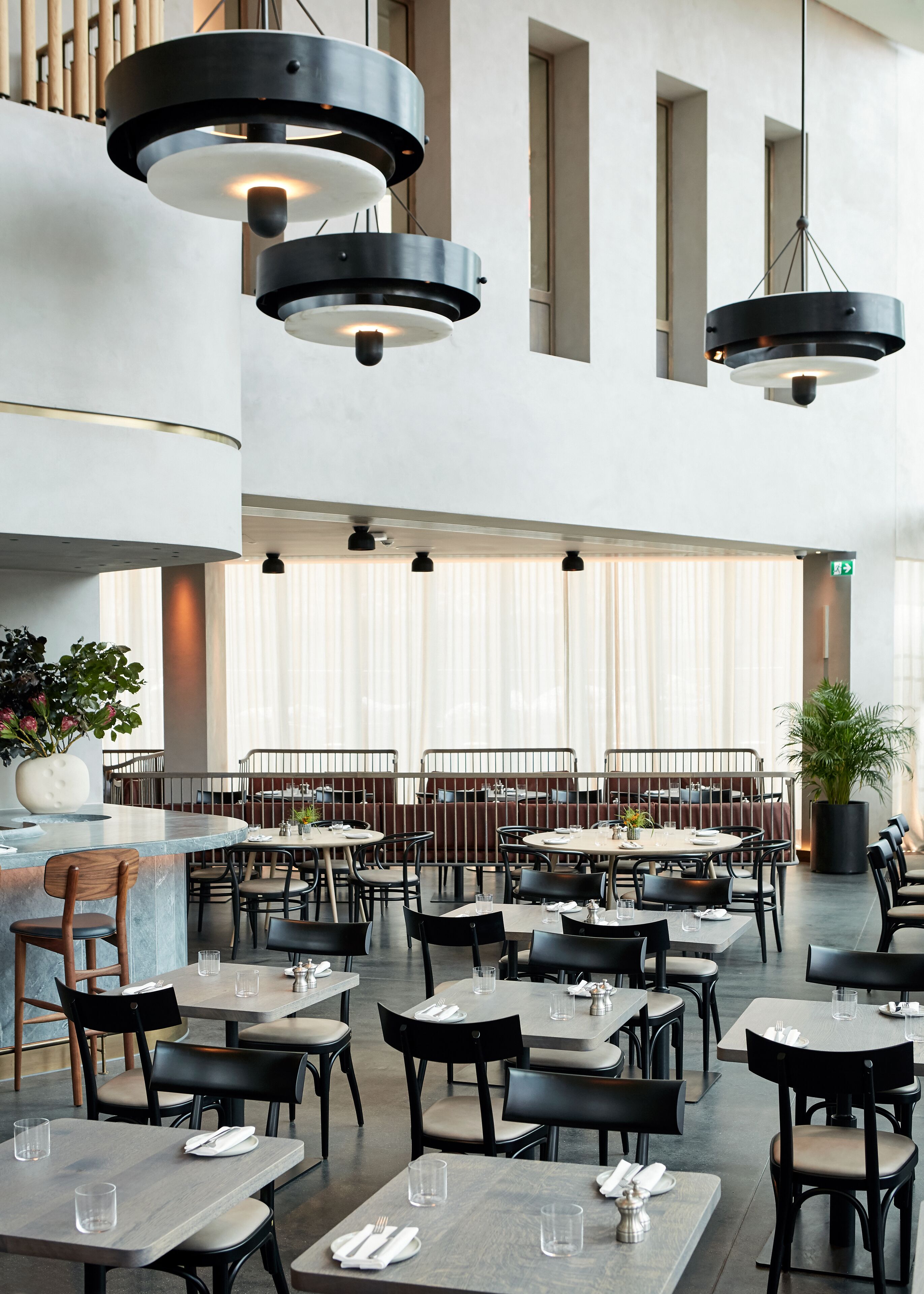 Un restaurante espacioso con varias mesas y sillas, moderna iluminación colgante y grandes ventanales que dejan entrar luz natural.