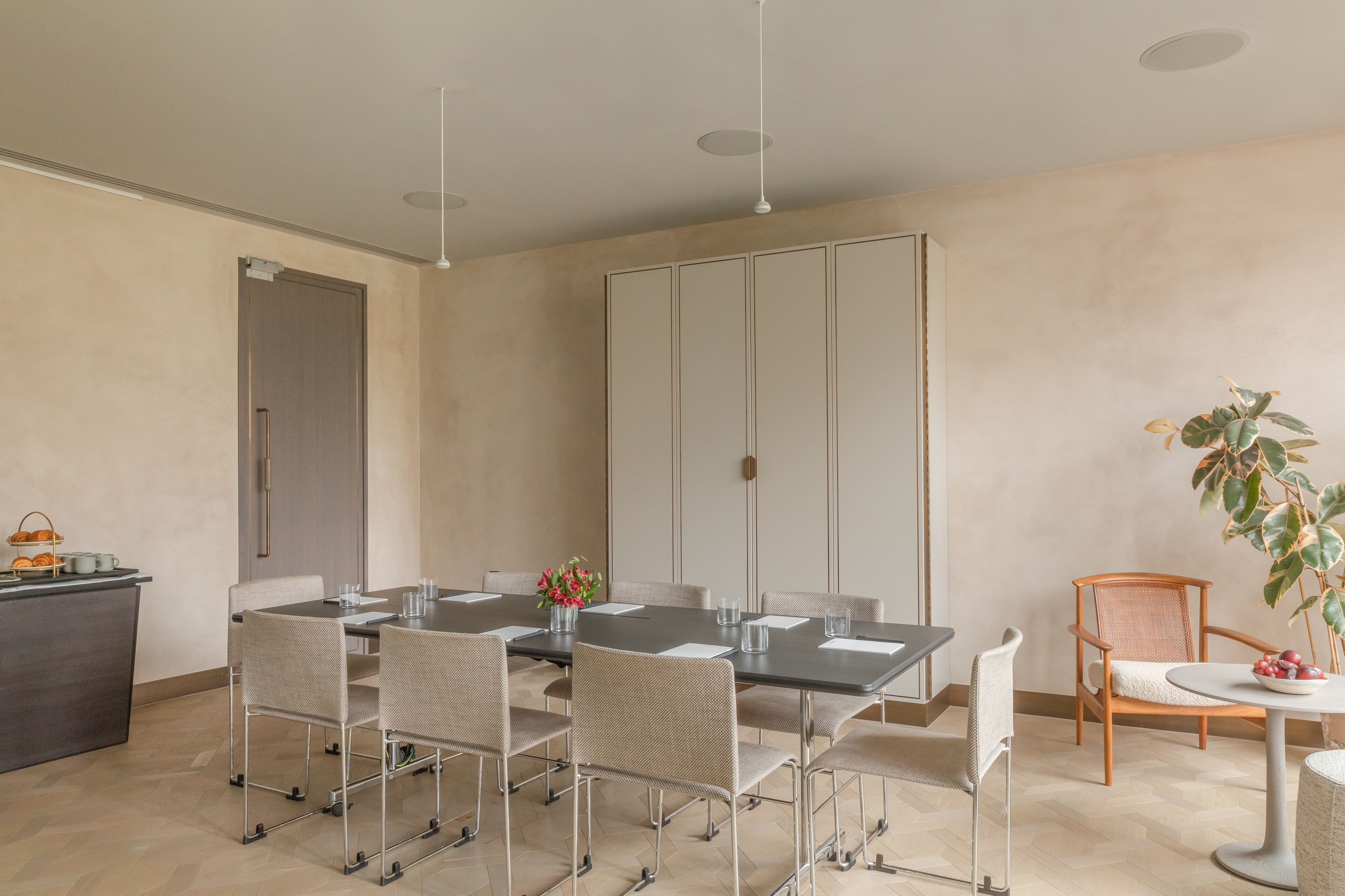 A modern dining area with a long table, multiple chairs, and a small side table with a plant.