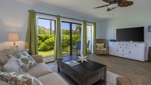 A living room with a sofa, coffee table, and a television on a cabinet. - Beautiful views of the mountains and oceans on the ground floor (Princeville)