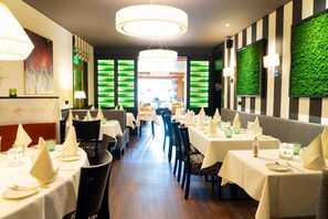 A restaurant with multiple tables, each set with white tablecloths and napkins, and chairs with patterned upholstery. - Hotel Restaurant Esser (Wegberg)