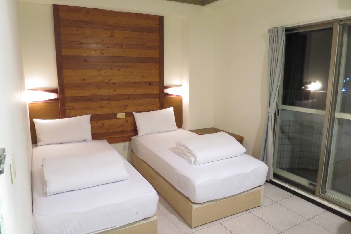 Two single beds with wooden headboards and white bedding, a window with curtains, and a tiled floor.