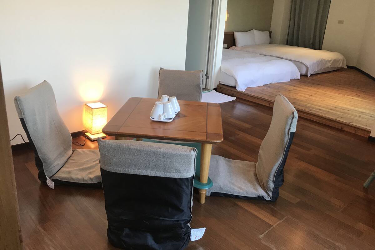 A hotel room with a wooden table, two chairs, a bed, and a nightstand with a lamp.