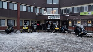 A hotel entrance with a sign reading "Shemon Suites Hotel" and several snowmobiles parked in front. - Shemron Suites Hotel (Deep River)