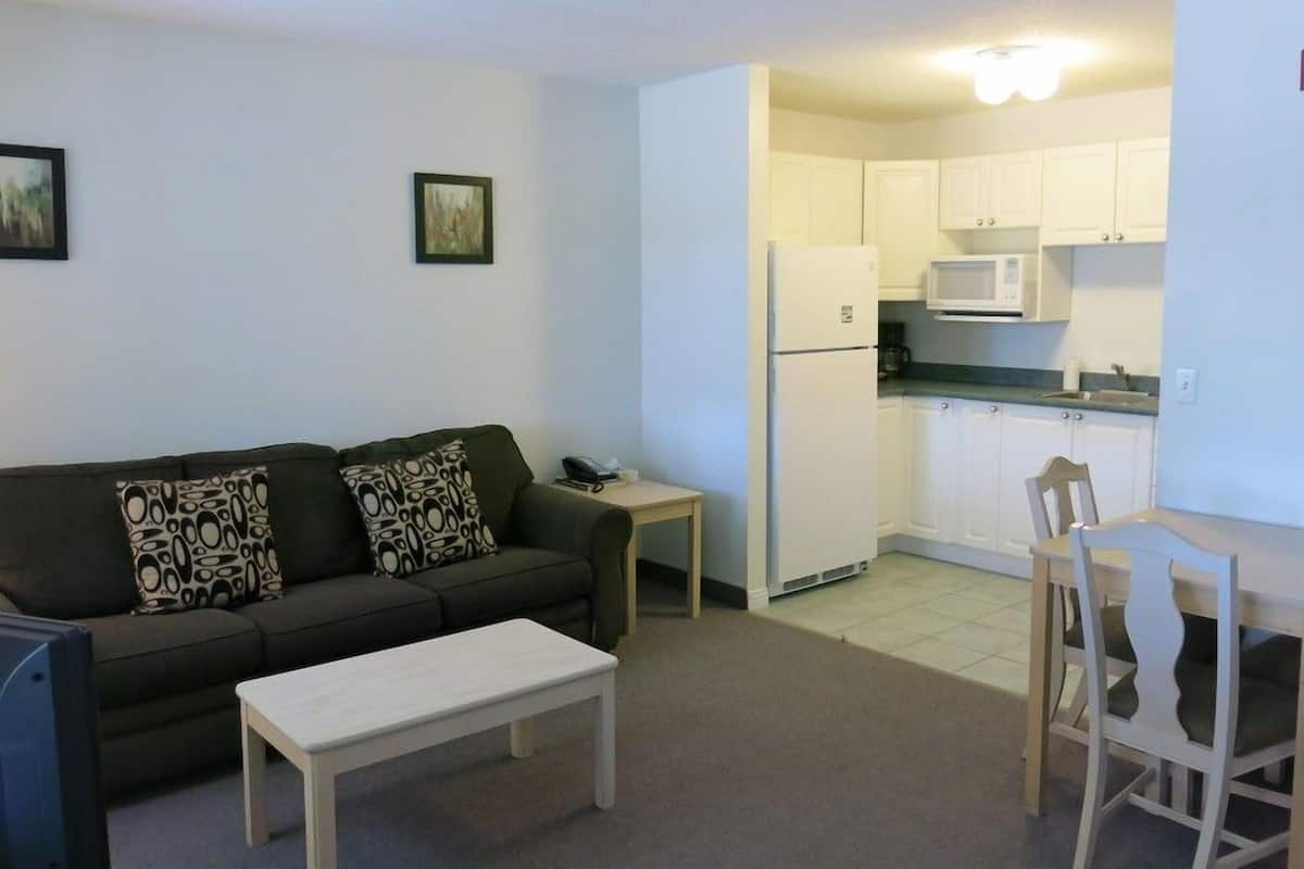 Un espacio habitable compacto con sofá, una mesita, zona de comedor con sillas y kitchenette con armarios y microondas.